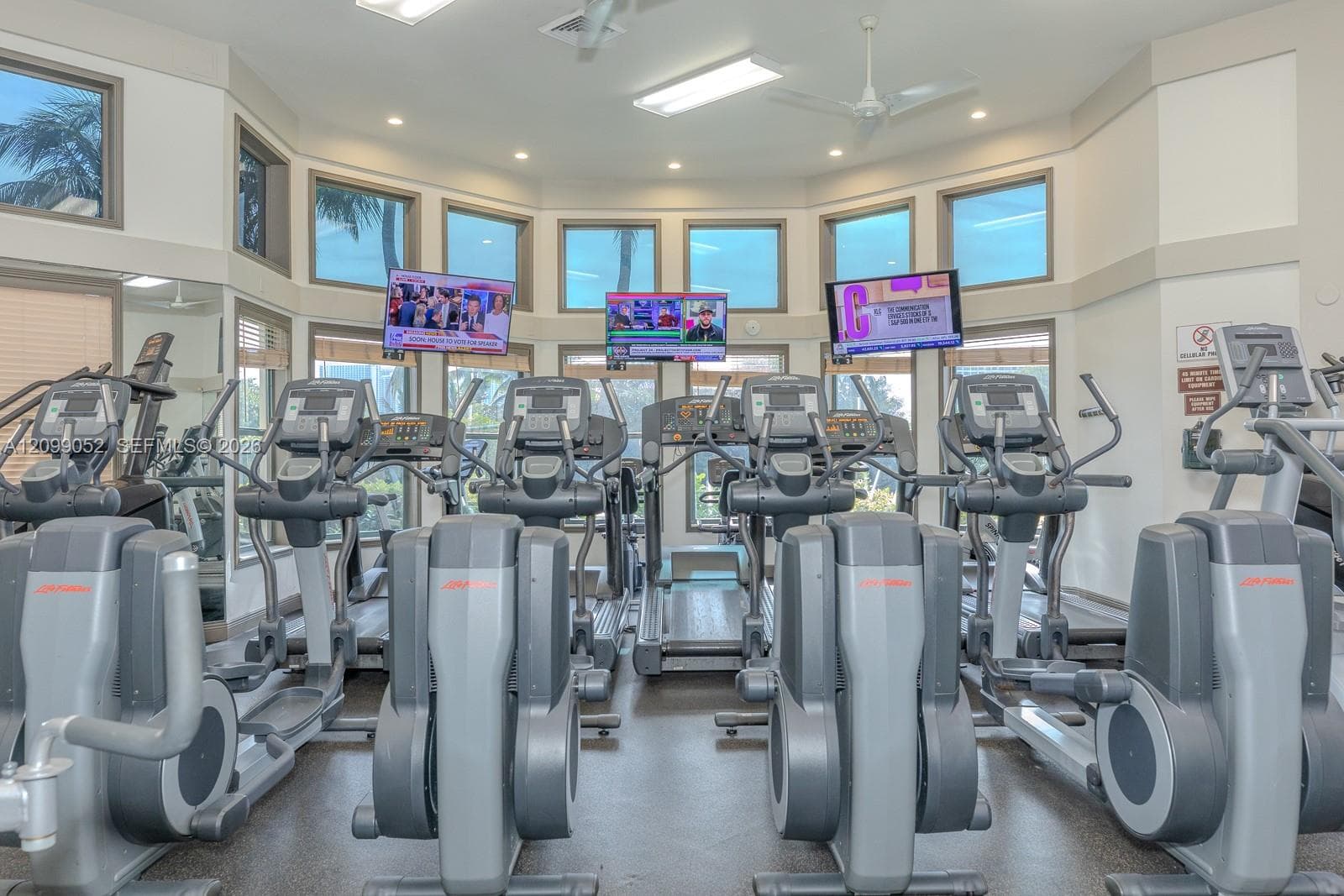 Fitness center featuring a curved wall of windows, multiple elliptical machines, treadmills, and ceiling-mounted televisions