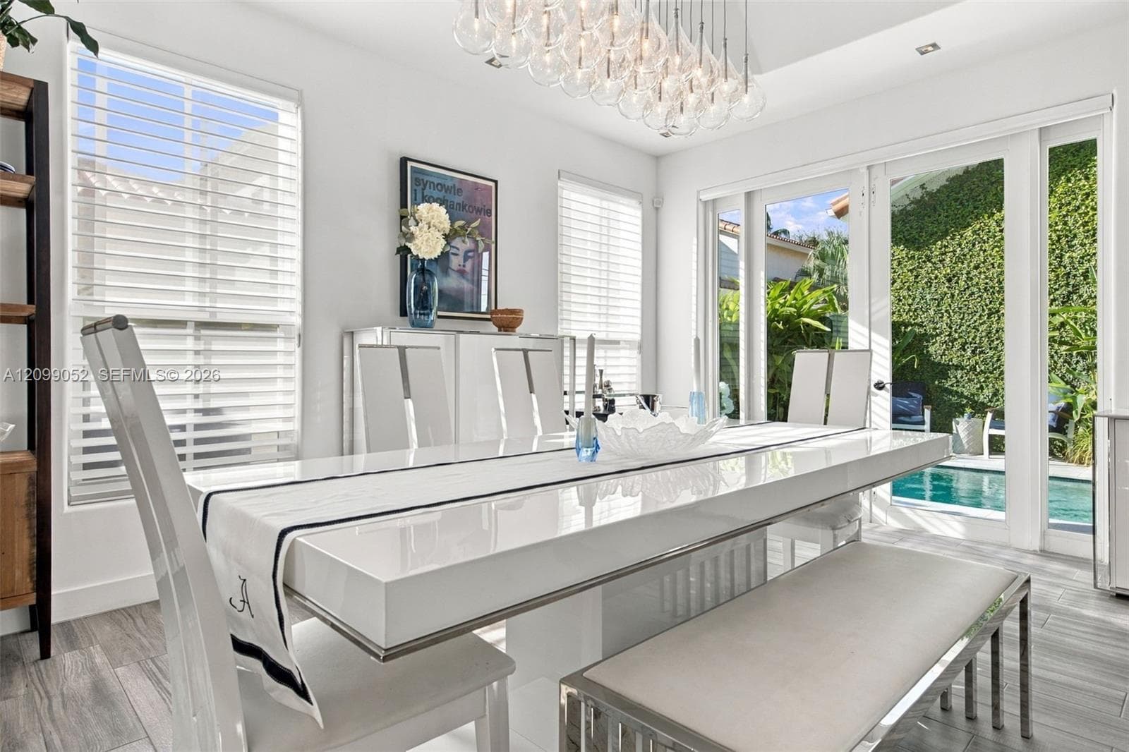 Dining area featuring large-format tile flooring, multi-globe chandelier, crisp white walls, horizontal window blinds, and glass doors opening to an outdoor swimming pool area