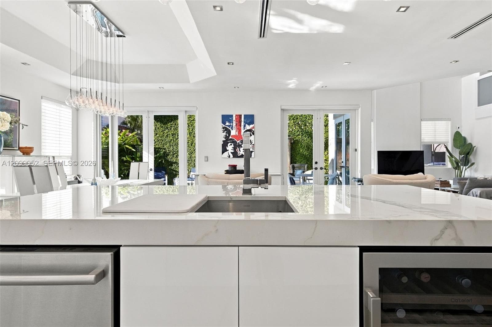 Kitchen island featuring a stone-look countertop, undermount sink with a high-arch faucet, built-in stainless steel dishwasher, integrated wine refrigerator, and minimalist flat-panel cabinetry