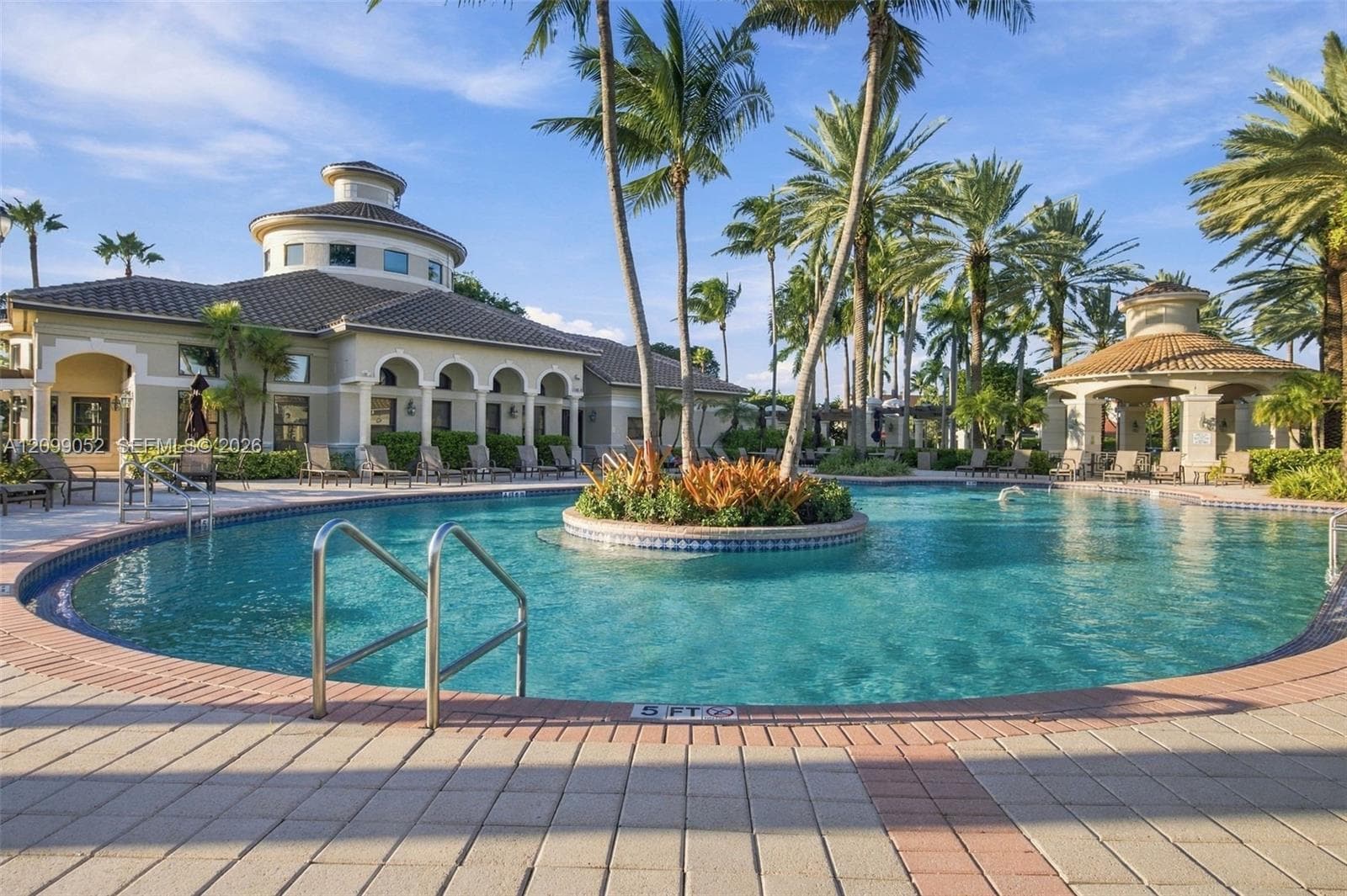 Community pool featuring a central island planter, stone paver decking, covered gazebo, and arched architectural detailing