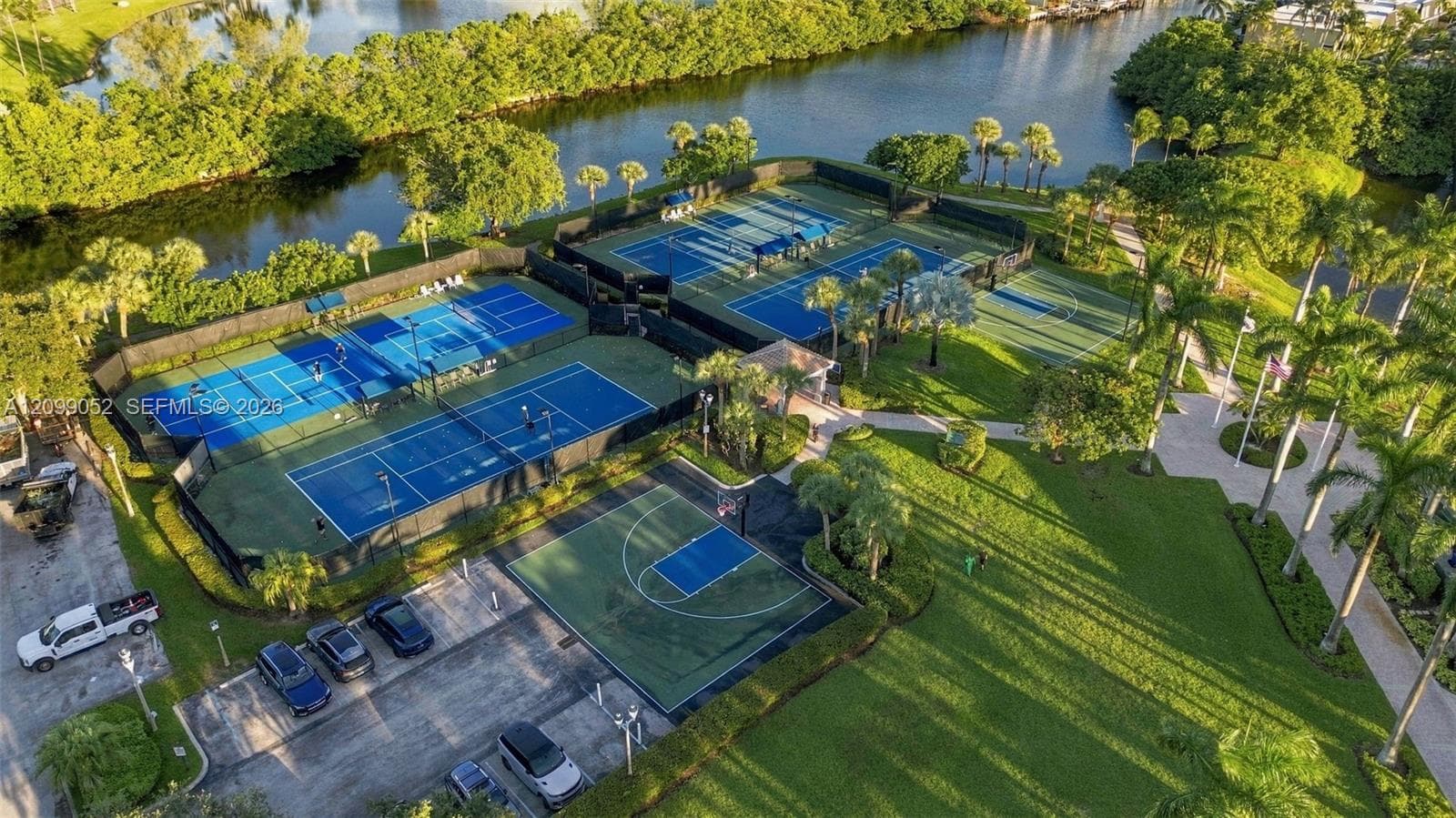 Recreational area featuring four tennis courts, a basketball court, paved walkways, and water frontage