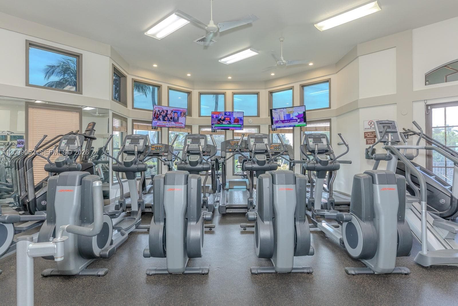 Fitness center featuring a high-vaulted ceiling, multiple rows of windows, rubberized flooring, and dual ceiling fans
