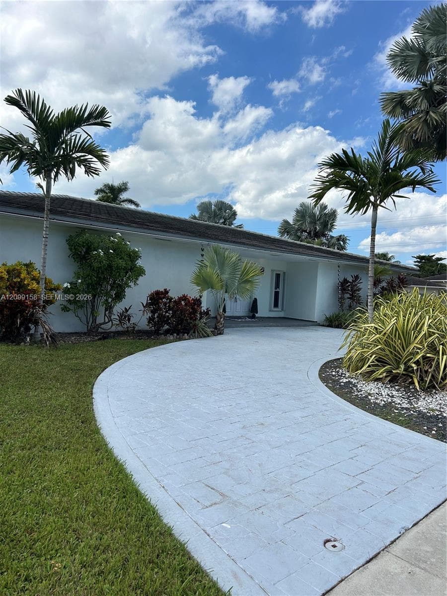 Single-story exterior featuring a light-colored stucco facade, a curved paver driveway, and mature palm tree landscaping