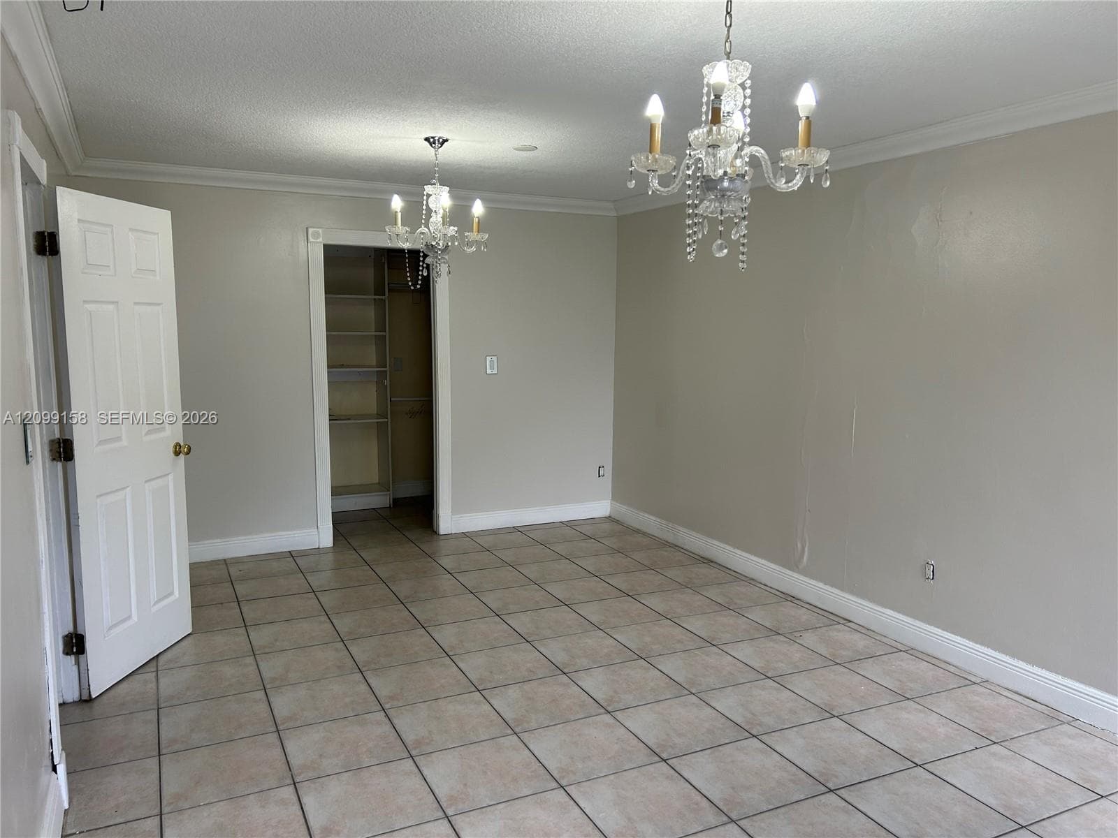 Room featuring neutral wall paint, tile flooring, two multi-tiered crystal chandeliers, and a walk-in closet with built-in shelving