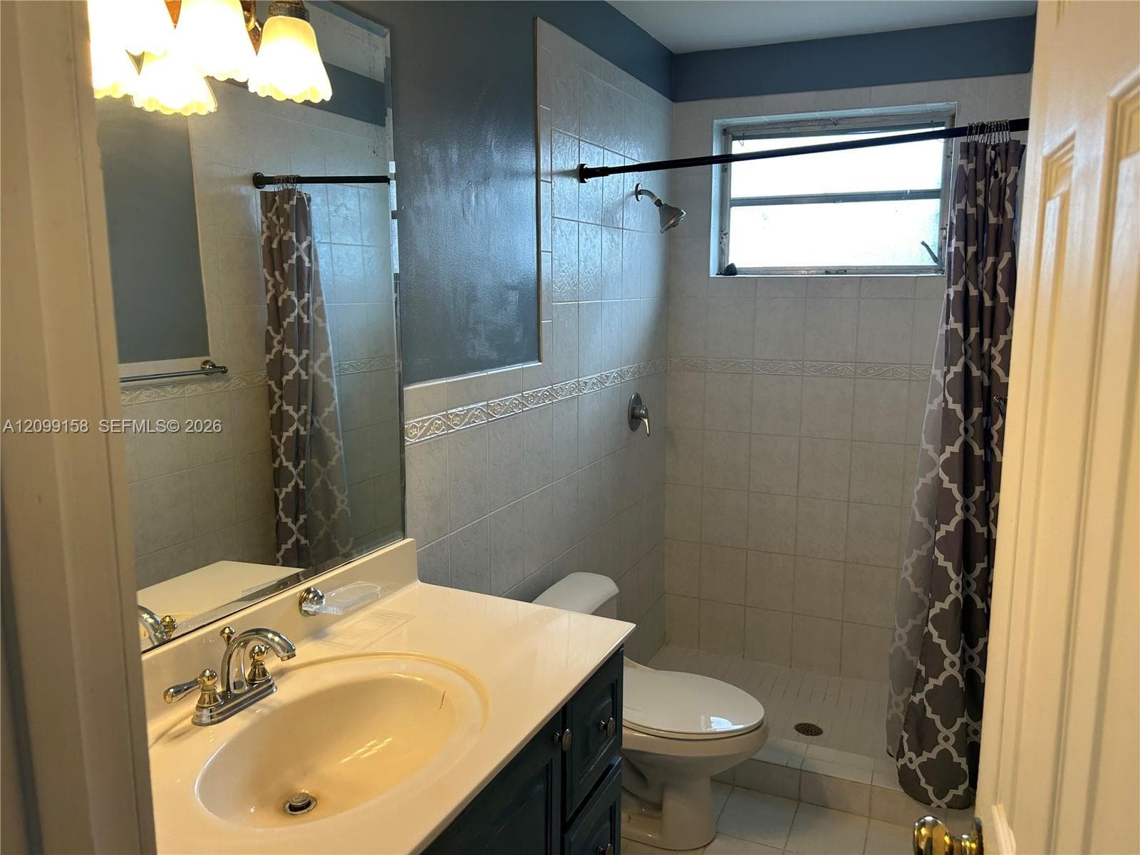 Bathroom featuring a dark-finish vanity with a light-toned countertop, integrated basin, wall-mounted mirror, and tile-surround shower with a glass window