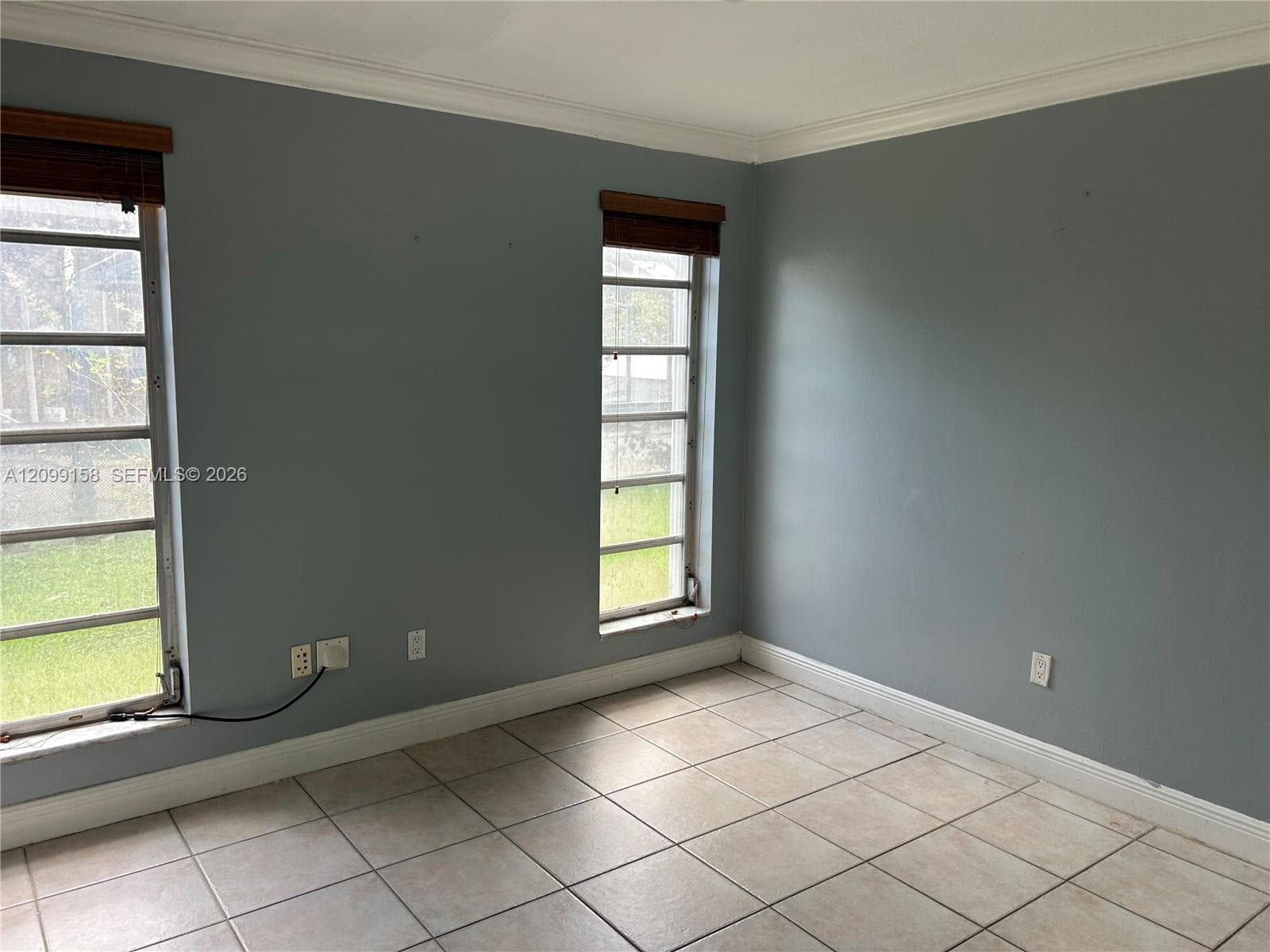 Room featuring neutral-toned ceramic tile flooring, crown molding, and two multi-pane windows with horizontal wood-finish blinds