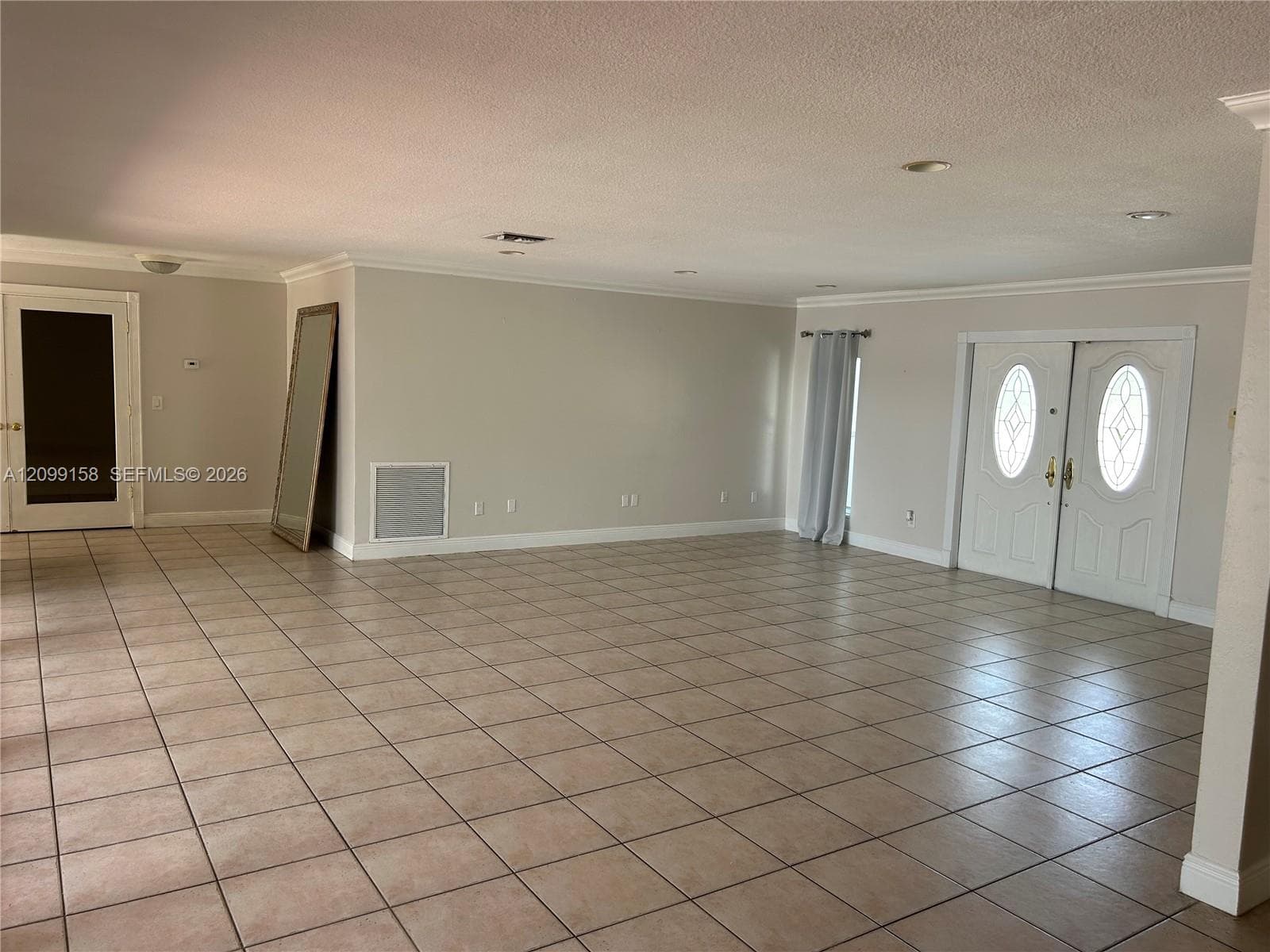Spacious open-concept living area with tile flooring throughout, recessed ceiling lighting, and multiple glass doors with sidelights providing natural illumination