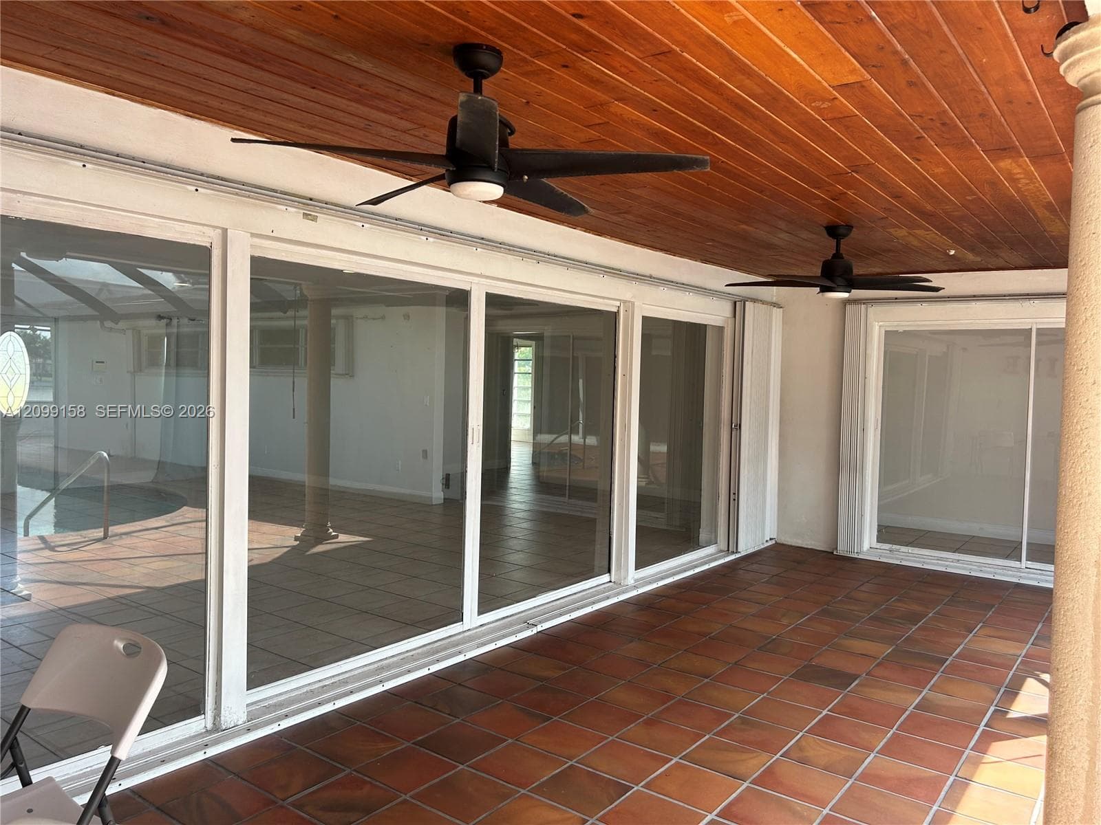 Covered outdoor patio featuring tile flooring, wood-plank ceiling, and dual ceiling fans, highlighted by expansive floor-to-ceiling sliding glass doors