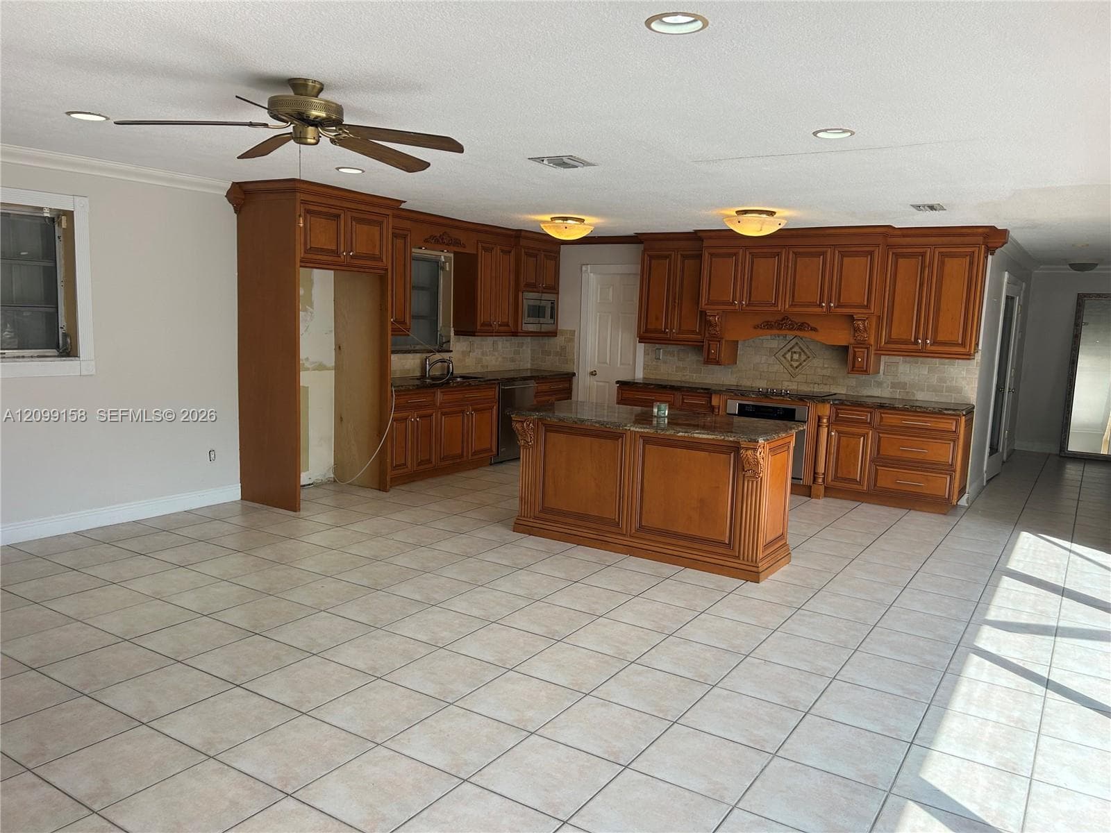 Kitchen featuring wood cabinetry, a central island with stone-finish countertops, tile flooring, and recessed lighting