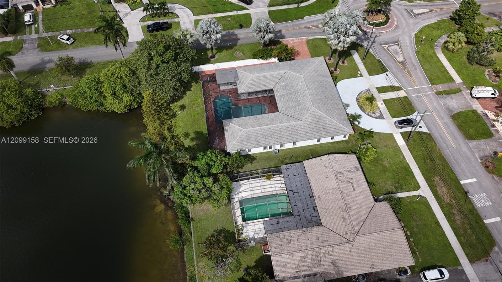 Aerial perspective of a property featuring a waterfront location, two screened-in pool enclosures, and mature landscaping
