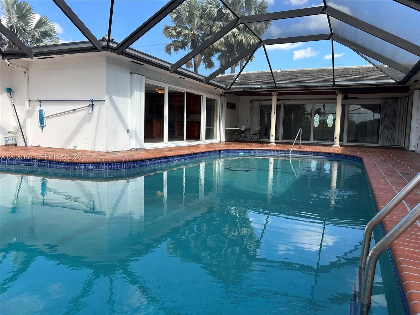 Screen-enclosed pool area featuring ceramic tile decking, built-in metal pool ladder, and multiple sets of sliding glass doors