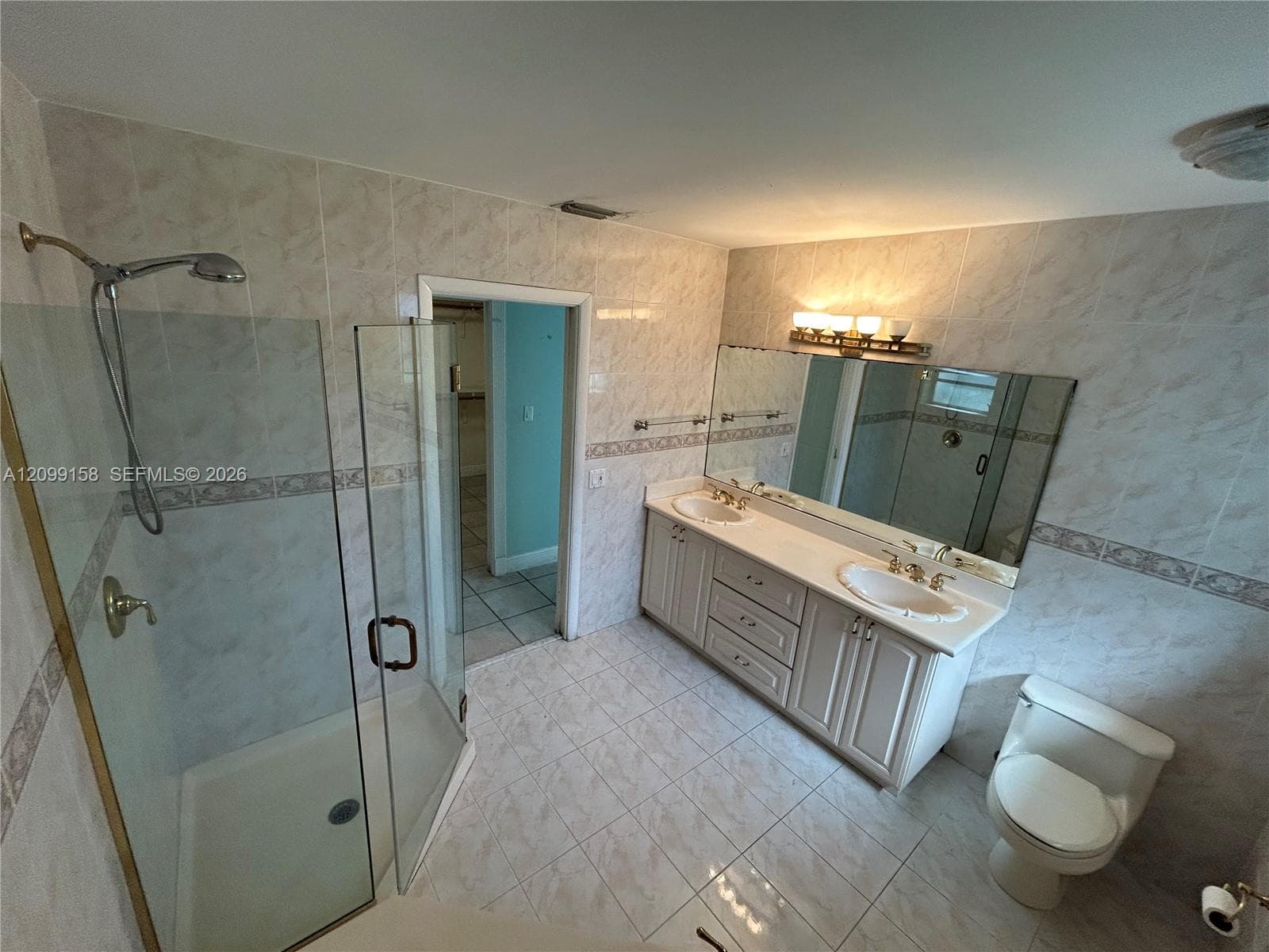 Bathroom featuring a double-sink vanity with light-toned cabinetry, an oversized wall-to-wall mirror, and a glass-enclosed shower with tiled walls