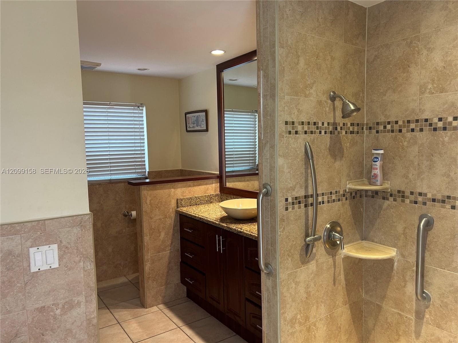 Walk-in shower featuring tiled walls with a mosaic accent border and stainless steel grab bars