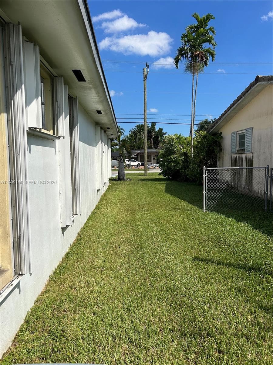 Exterior side yard featuring a grass lawn, chain-link fencing, and mature palm trees