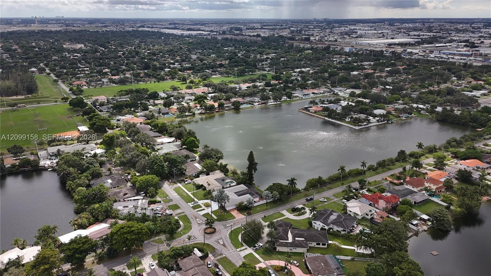 Aerial perspective featuring extensive lake frontage, paved neighborhood streets, and established mature landscaping
