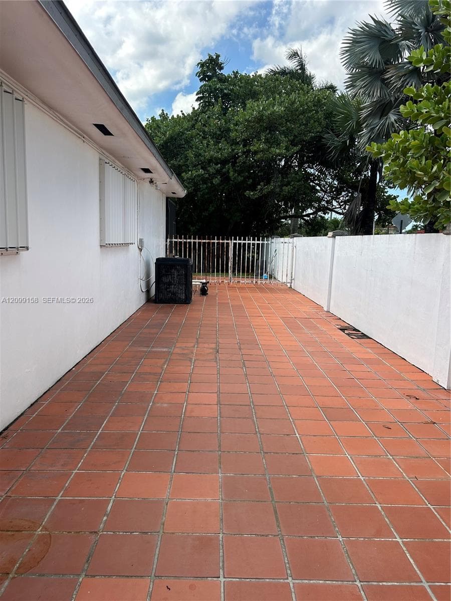 Exterior side patio featuring terracotta tile flooring, enclosed by a white masonry privacy wall and gated metal fencing