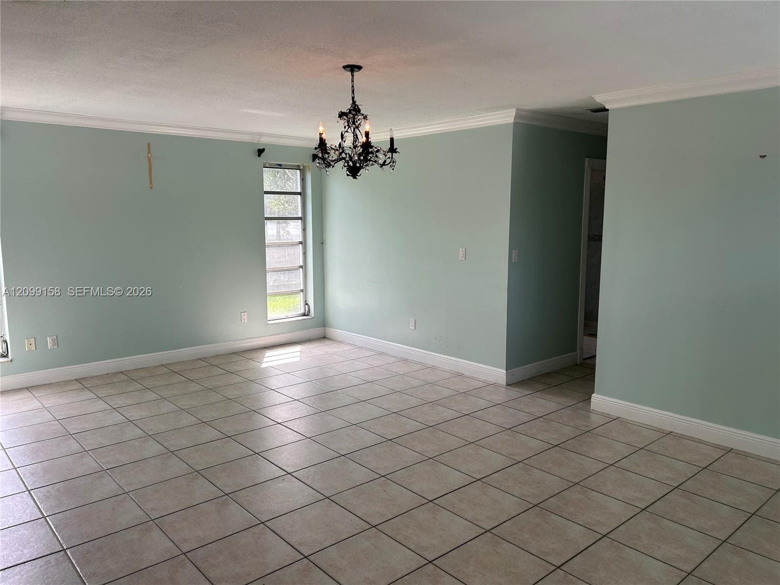 Spacious interior featuring large-format tile flooring, crown molding, multi-pane windows, and a decorative wrought iron chandelier