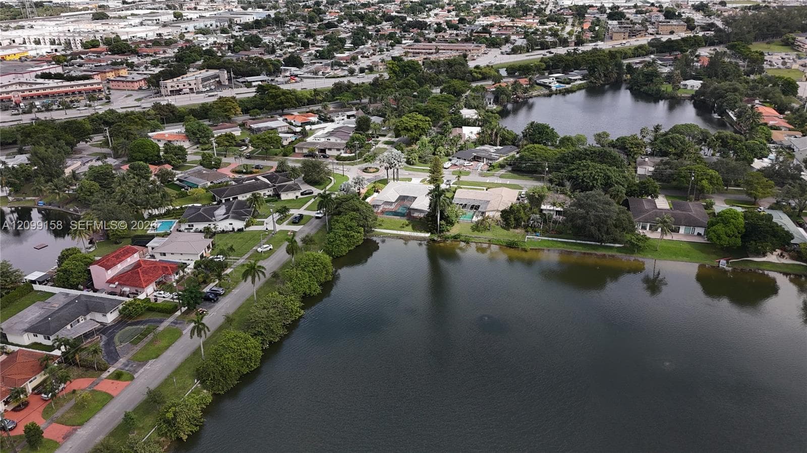 Aerial perspective featuring expansive waterfront positioning, mature palm trees, residential paved streets, and established neighborhood landscaping