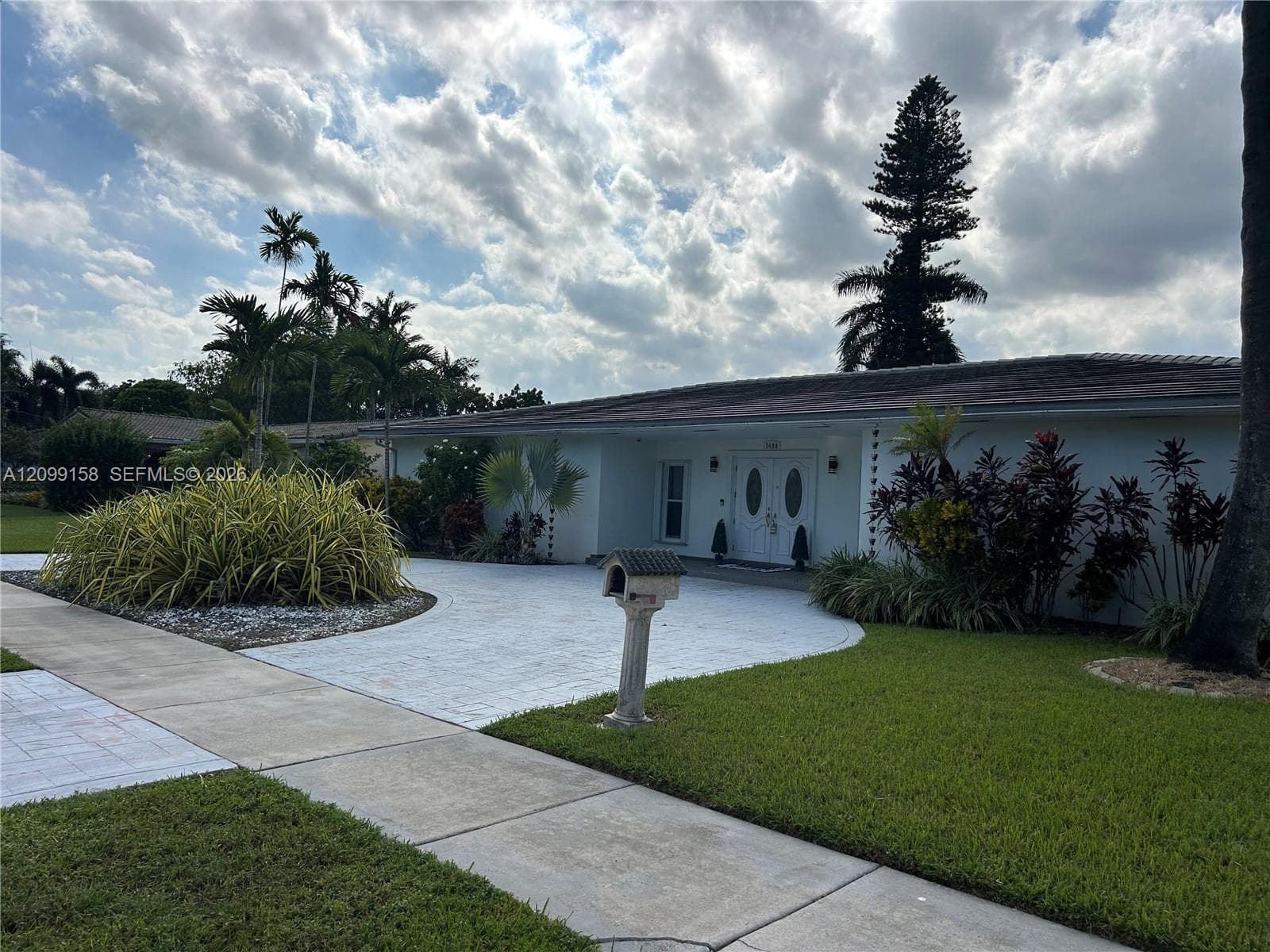Single-story residence featuring a paved circular driveway, double-door entry with oval glass inserts, and lush professional landscaping