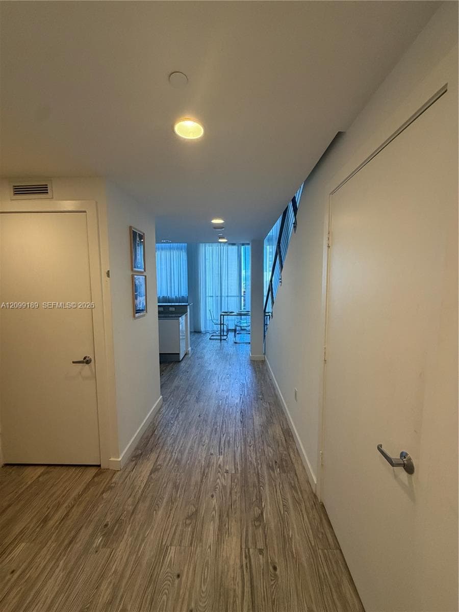 Interior hallway featuring wood-finish flooring, flush-mount ceiling lighting, and a staircase with metal railings