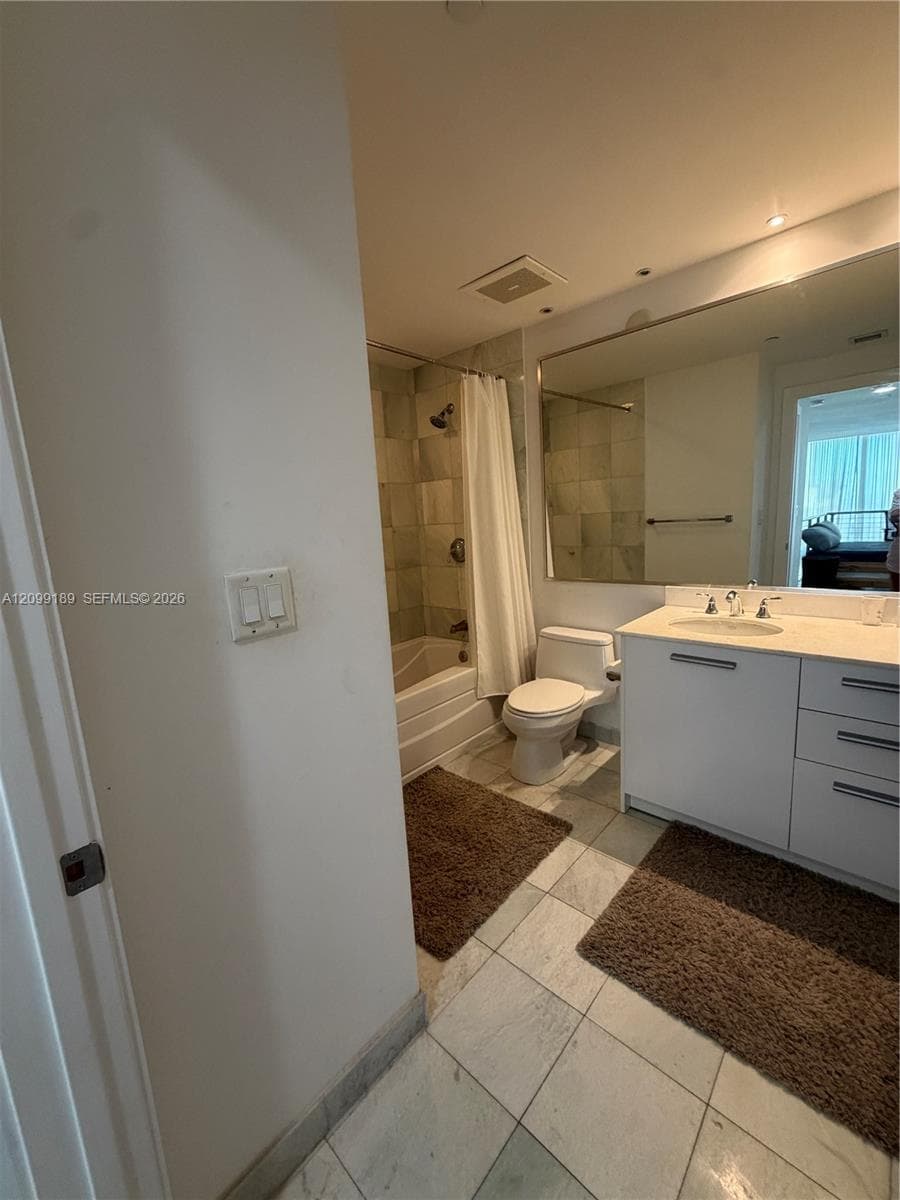 Bathroom featuring stone-finish flooring, a vanity with a light-toned countertop and integrated sink, a large wall-mounted mirror, and a tub-shower combination with tile surround