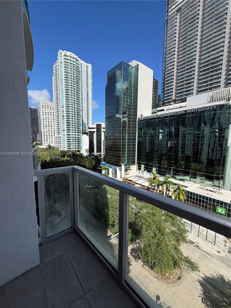 Private balcony featuring glass panel railing, tiled flooring, and a metropolitan cityscape
