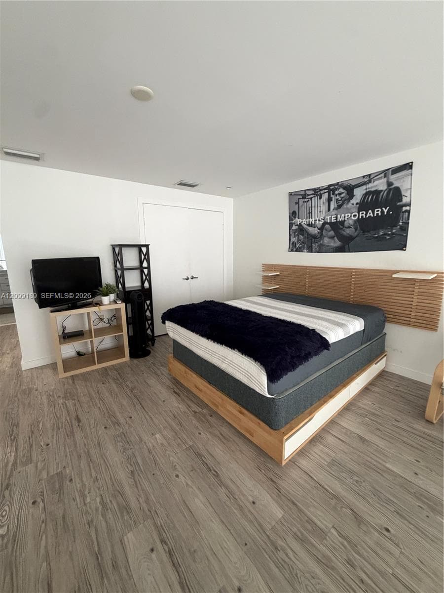 Room featuring wood-finish flooring, a mounted slatted wood headboard with integrated shelving, and double-door closet storage