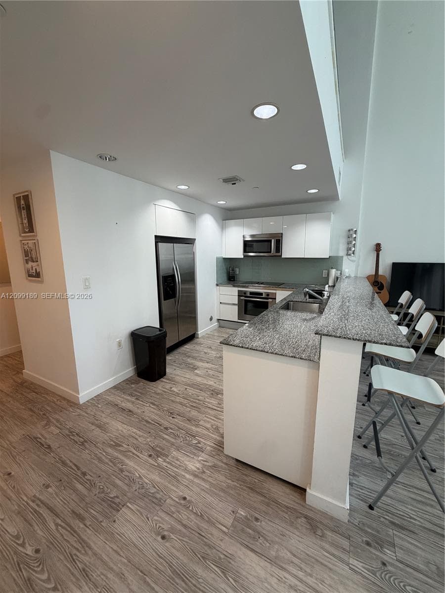 Kitchen featuring high-gloss cabinetry, stone-surface breakfast bar, stainless steel appliances, and wood-finish flooring