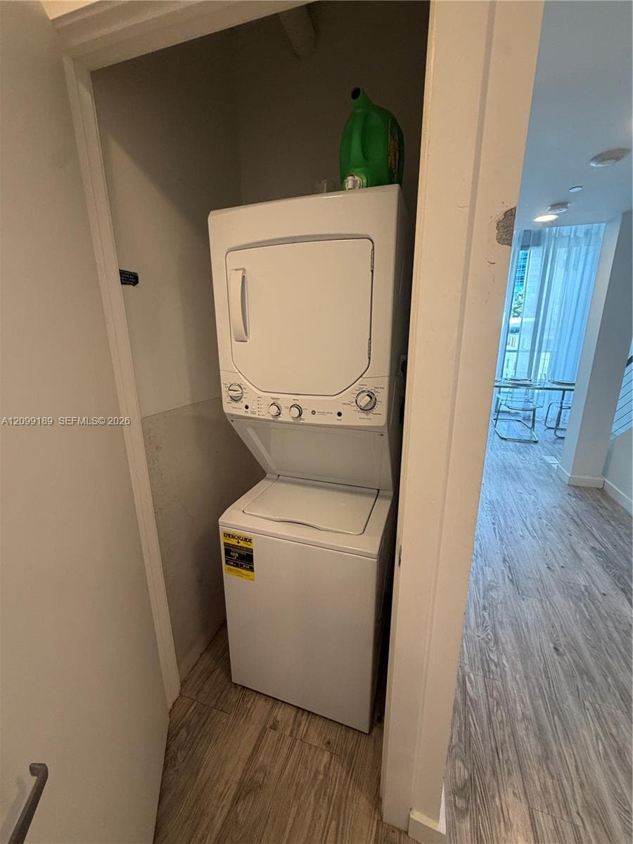 Dedicated laundry closet featuring a stackable white washer and dryer unit and wood-finish flooring