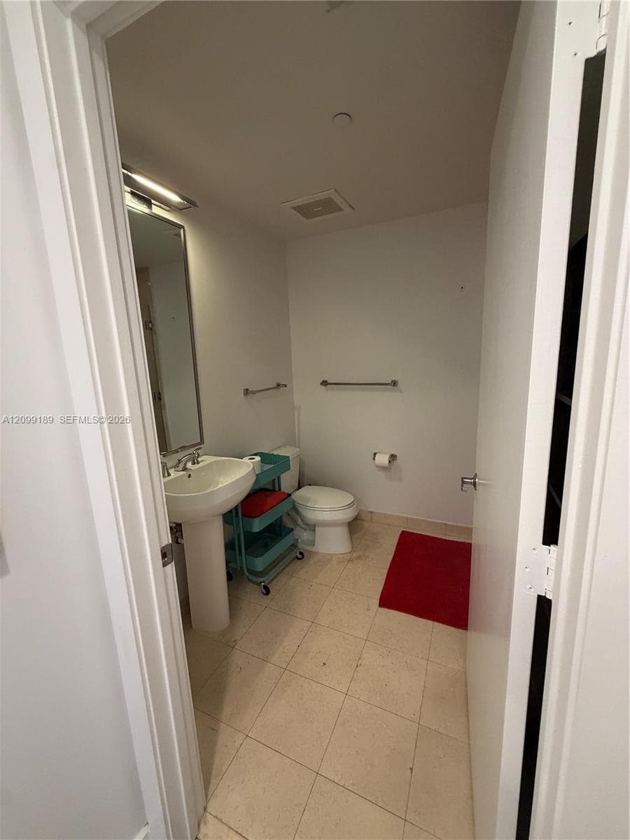 Bathroom featuring a pedestal sink, wall-mounted mirror with integrated lighting, ceramic tile flooring, and metallic hardware fixtures