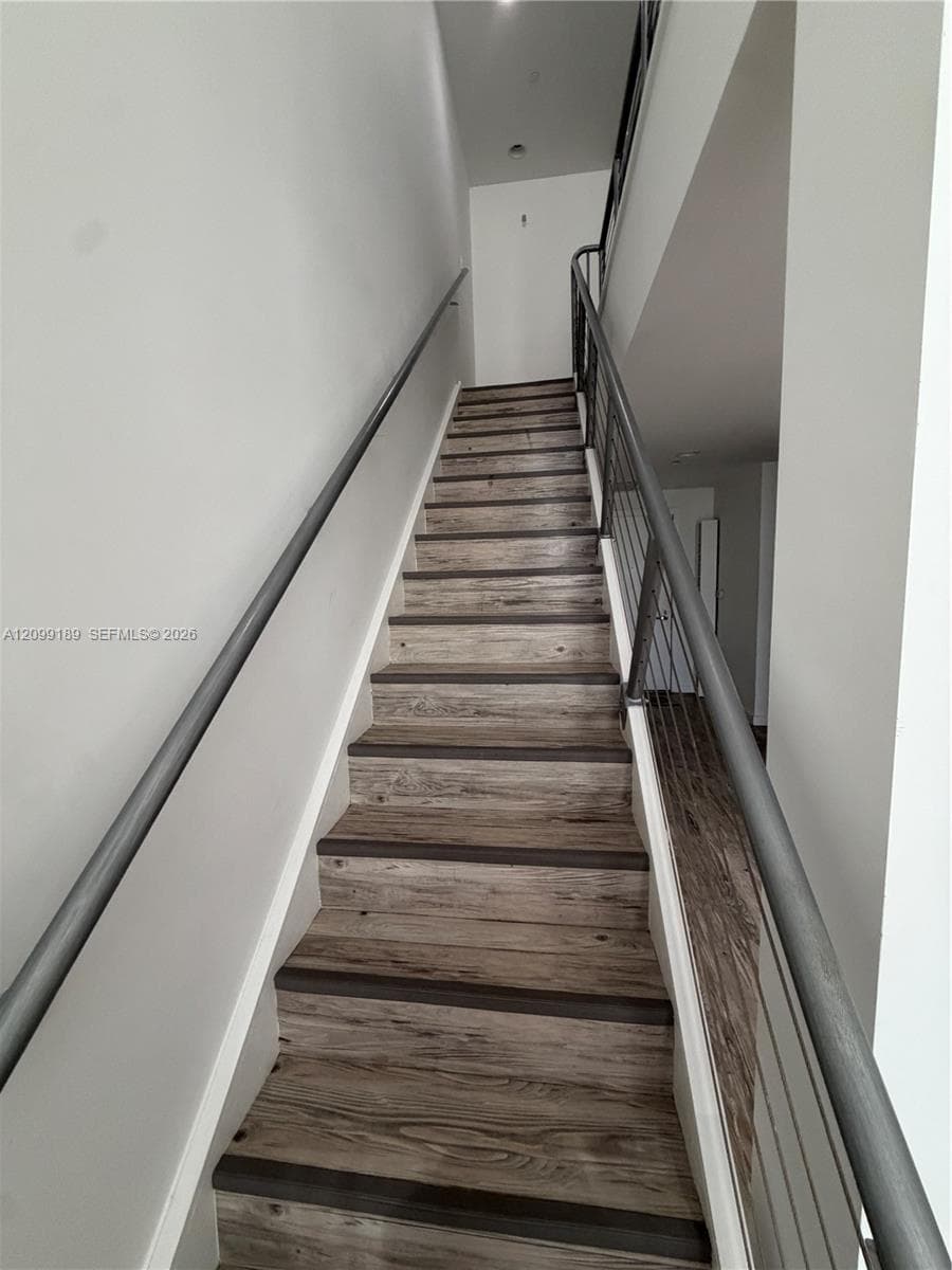 Staircase featuring wood-finish treads, a metal handrail, and a vertical cable railing system