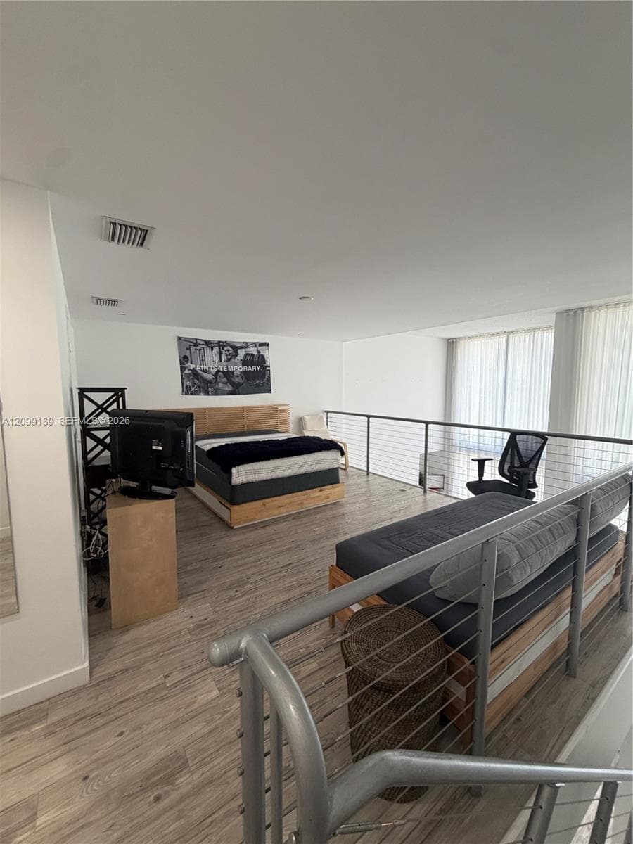 Open-concept loft area featuring wood-finish flooring, metal cable railing, and floor-to-ceiling windows with vertical blinds