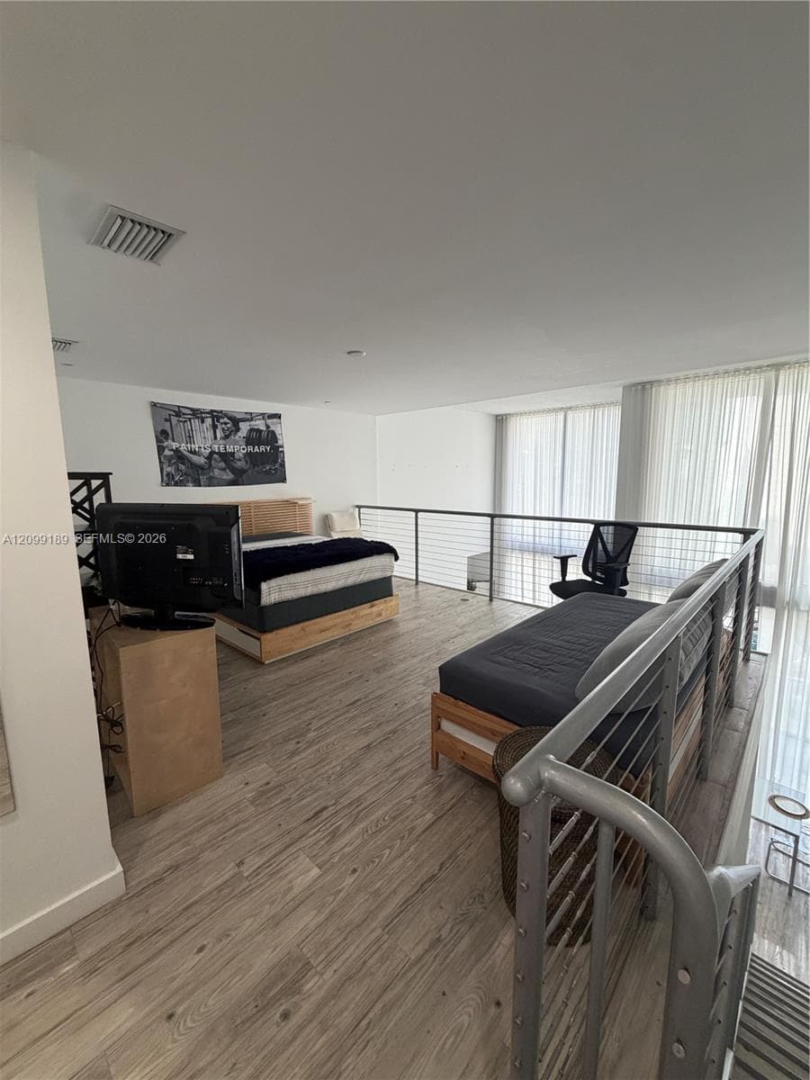 Open-concept loft area featuring wood-finish flooring, metal cable railing, and floor-to-ceiling windows