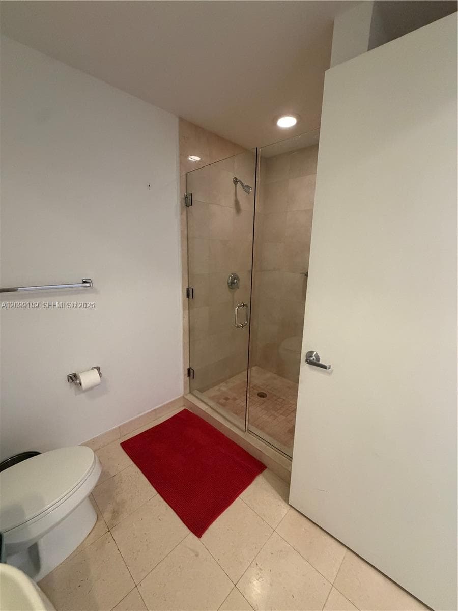 Walk-in shower with frameless glass door, tile surround, and chrome shower fixture, complemented by light-toned tile flooring