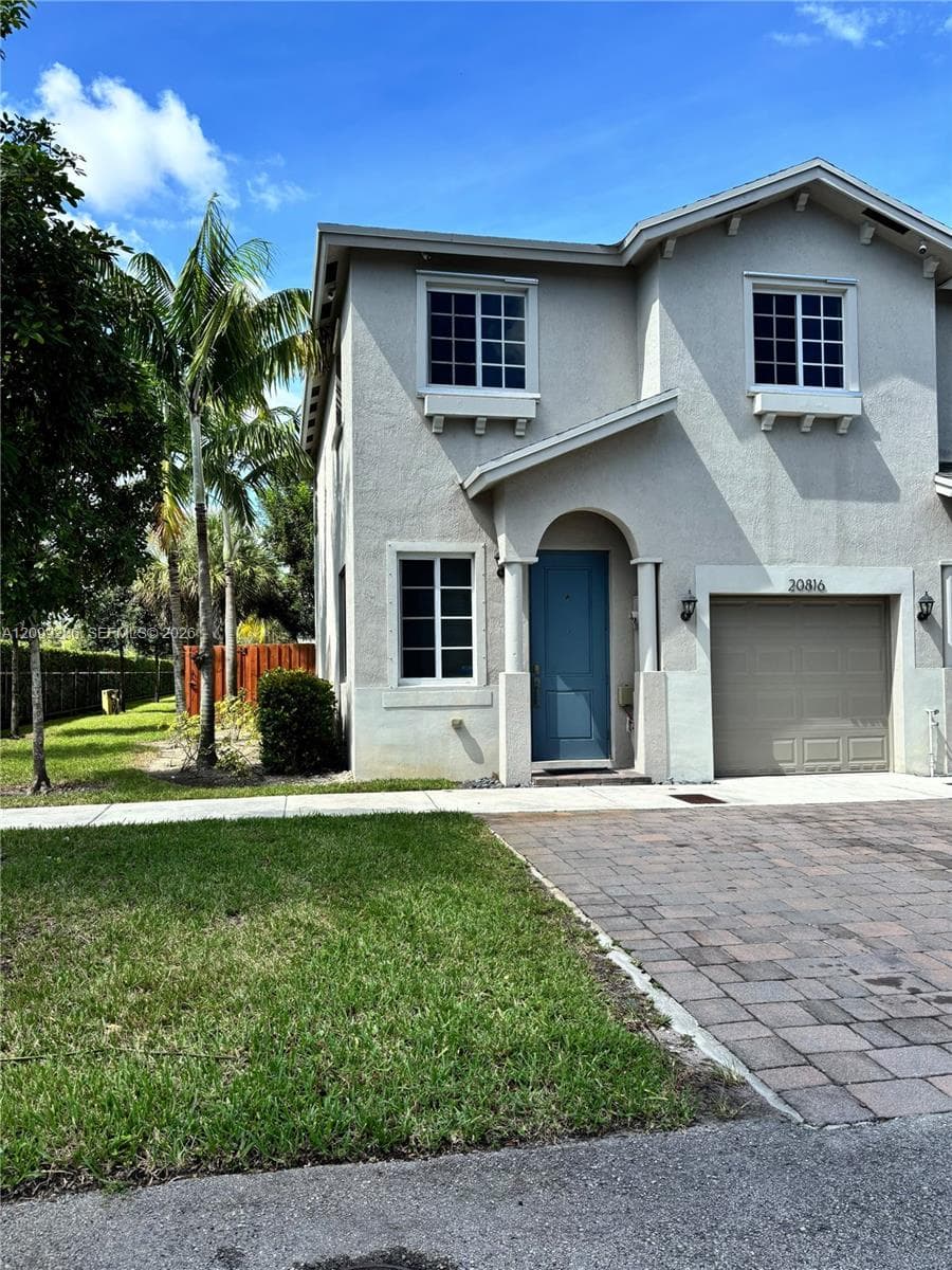 Two-story exterior featuring a stucco facade, arched entryway, single-car garage, multi-pane windows with decorative molding, and a paved stone driveway