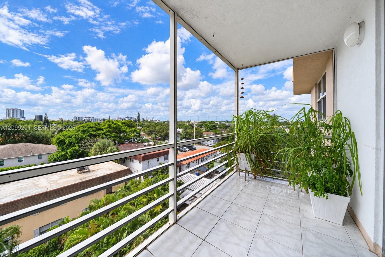 Balcony with tile flooring and a white metal railing, offering a cityscape and tree canopy backdrop