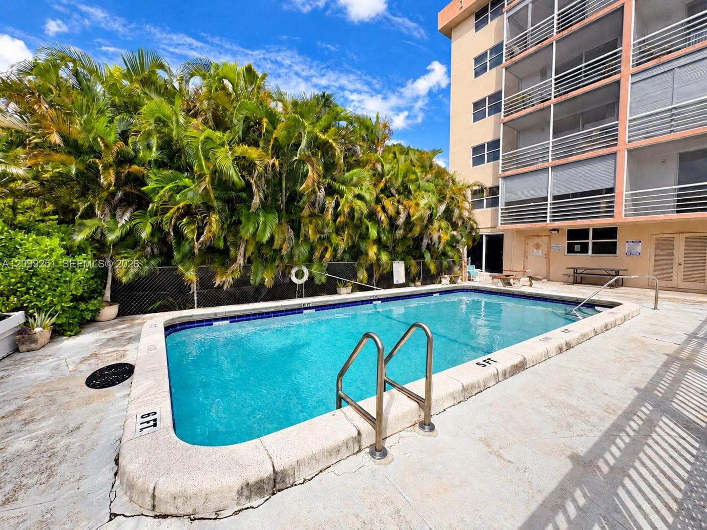 Outdoor swimming pool with integrated steps, surrounded by a concrete deck, and lush tropical landscaping