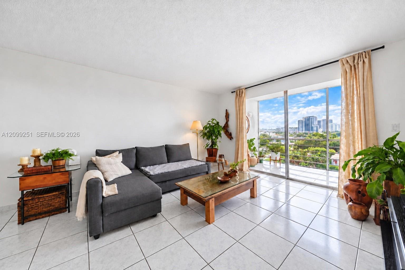 Bright, open living area showcasing tile flooring, expansive glass sliding doors with natural light, and a charcoal upholstered sectional sofa
