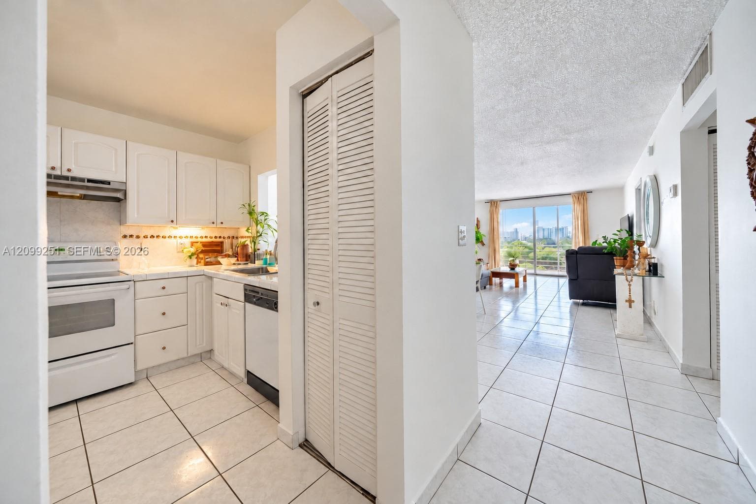 White kitchen cabinetry, white appliances, tile flooring, louvered bi-fold door, and sliding glass door to exterior