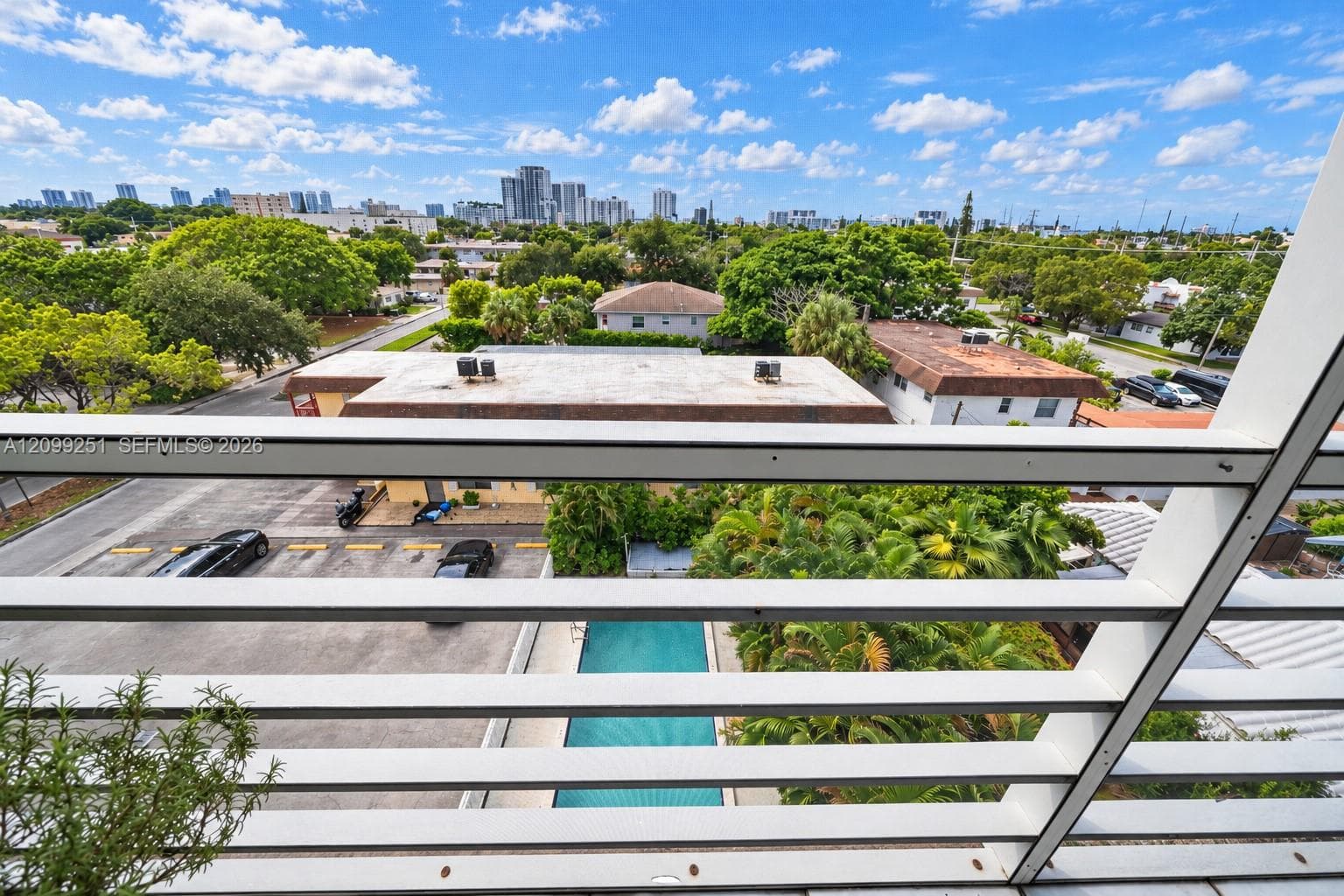 Outdoor balcony with slatted railing overlooking a cityscape and a rectangular swimming pool