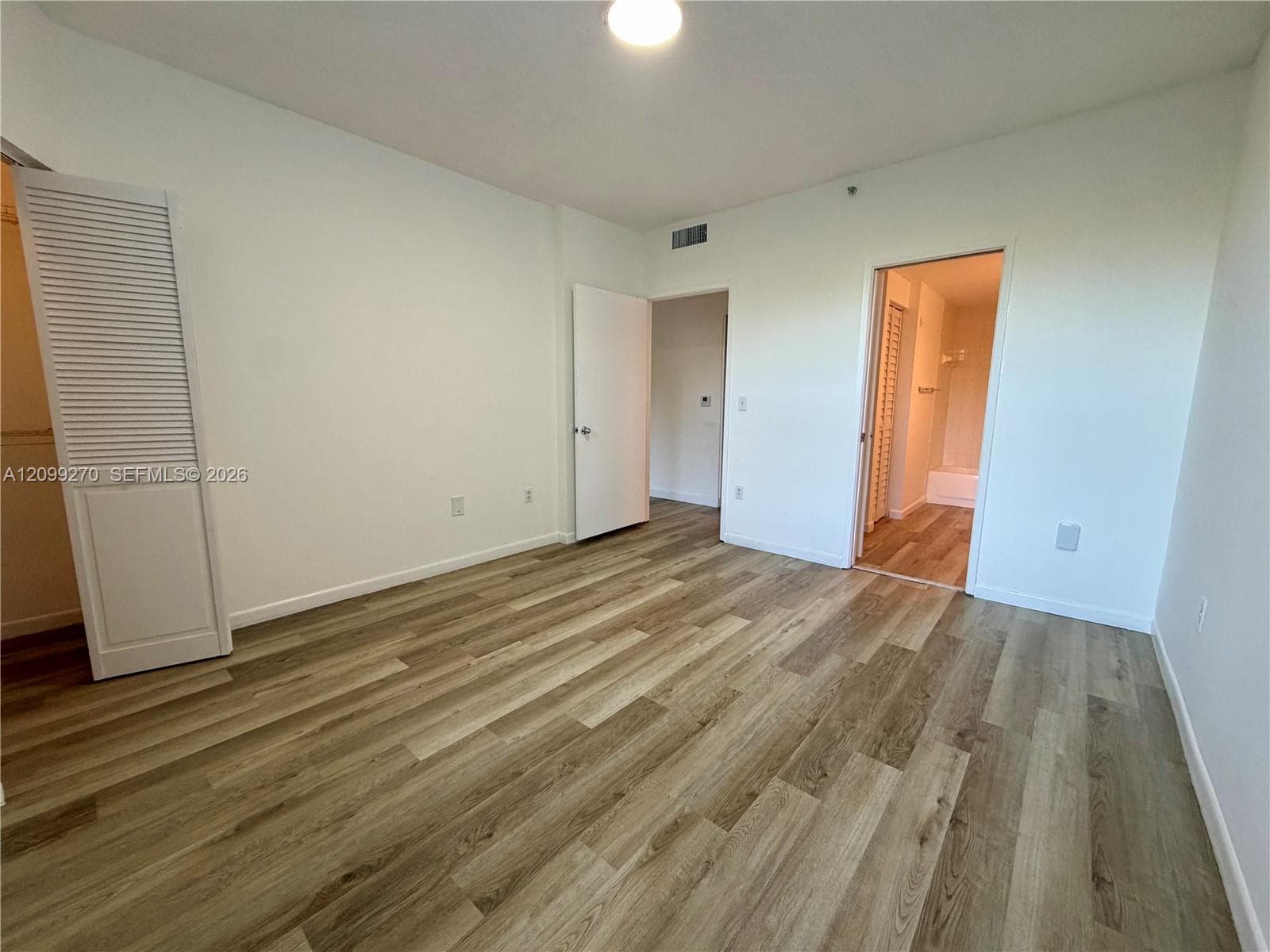 Room featuring wood-finish flooring, white walls, louvered closet doors, and recessed ceiling lighting