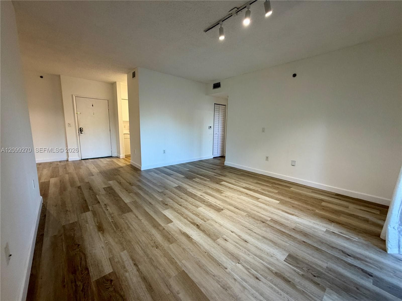 Open floor plan featuring wood-finish flooring, neutral wall paint, and ceiling-mounted track lighting