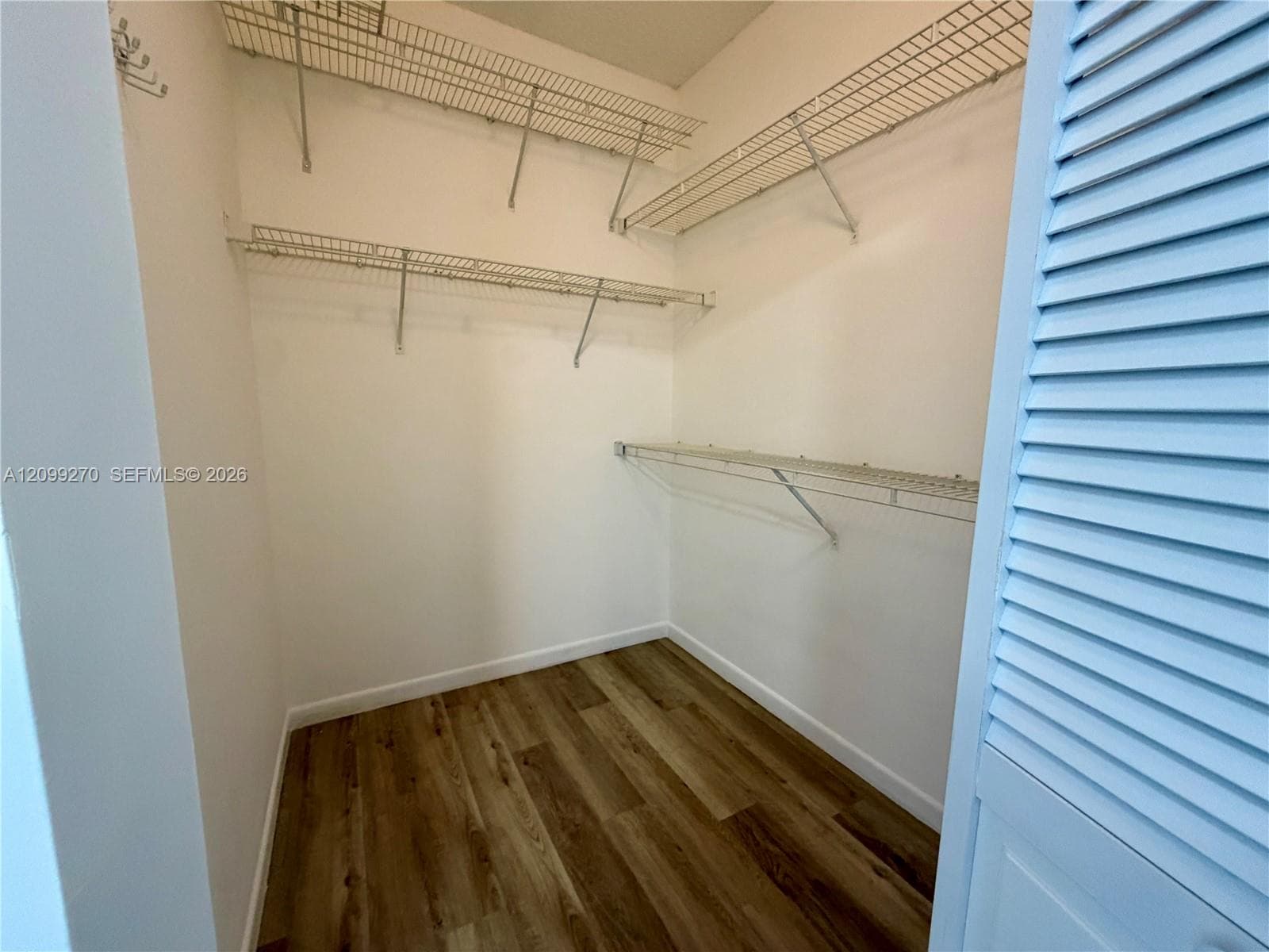Walk-in storage space featuring wood-finish flooring, multi-level wire shelving, and louvered door access