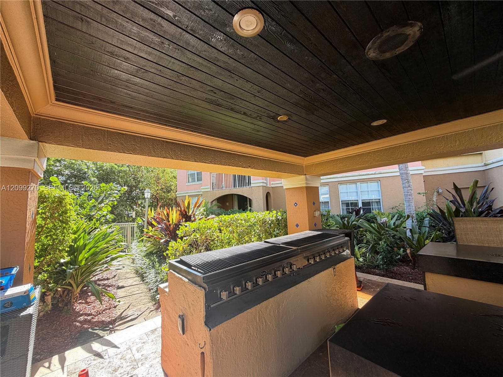 Covered outdoor kitchen featuring built-in gas grill, smooth-stucco island, dark wood-plank ceiling, and recessed lighting