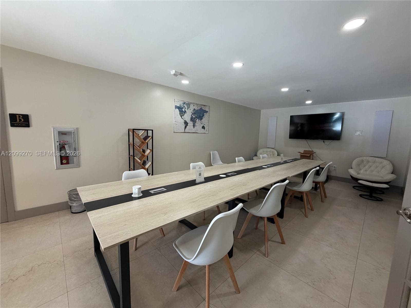 Large-scale meeting room featuring tile flooring, recessed lighting, and a long built-in wood-finish conference table with integrated power ports and a black center inlay