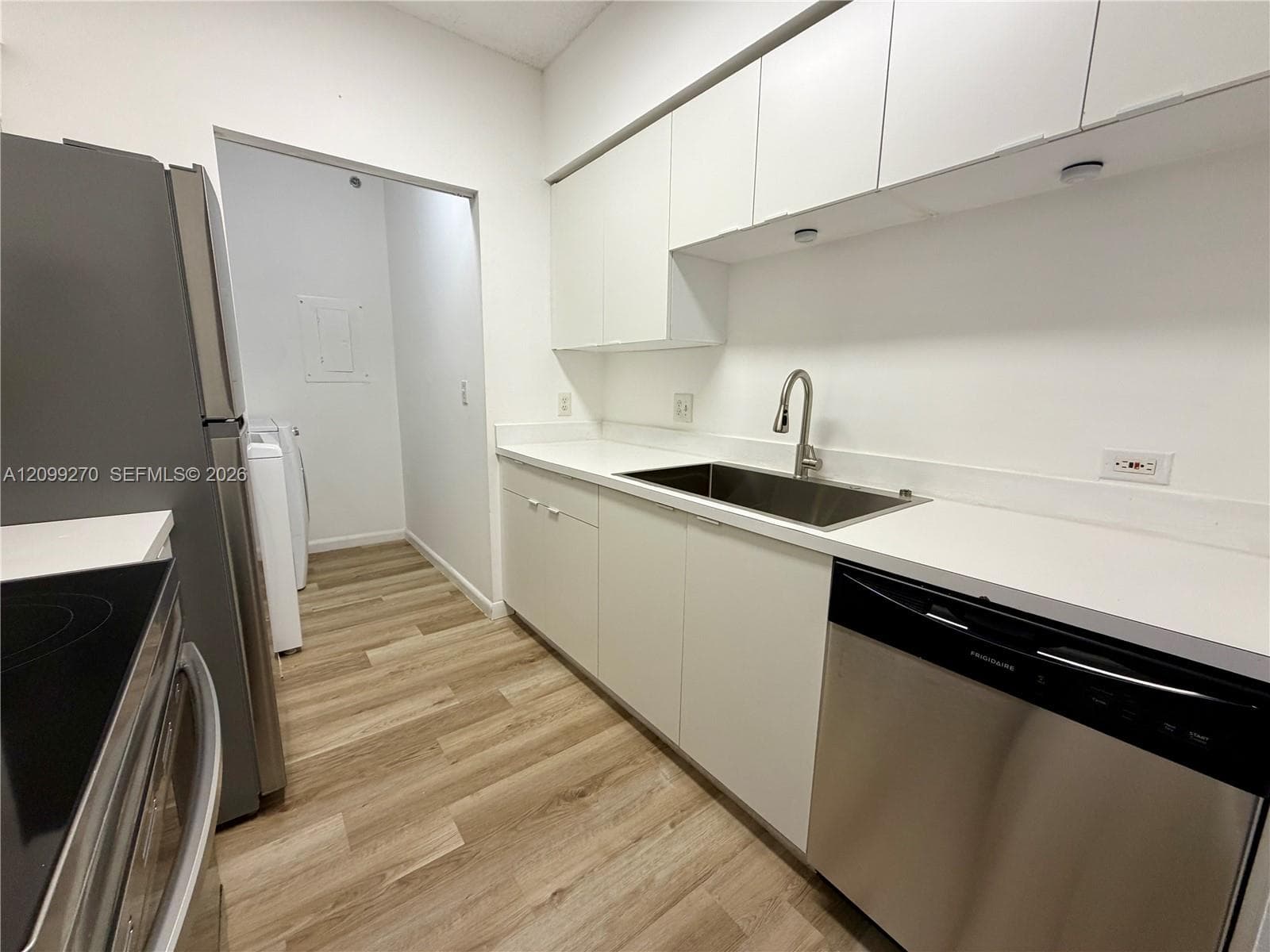 Kitchen featuring white flat-panel cabinetry, solid-surface countertops, a stainless steel undermount sink with a gooseneck faucet, stainless steel dishwasher, and wood-finish flooring