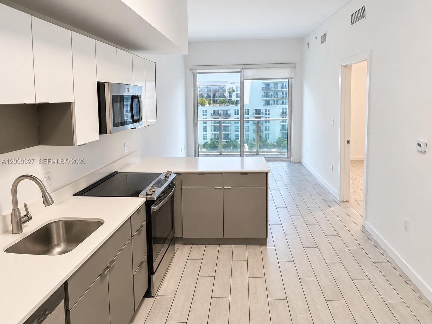 Kitchen featuring flat-panel cabinetry, light-toned countertops, stainless steel appliances, and large-format tile flooring, complete with a glass door to a balcony