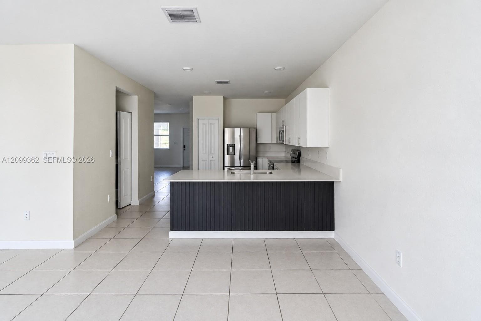 Kitchen featuring white cabinetry, a peninsula with vertical slat detailing, light-toned countertops, tile flooring, and stainless steel appliances
