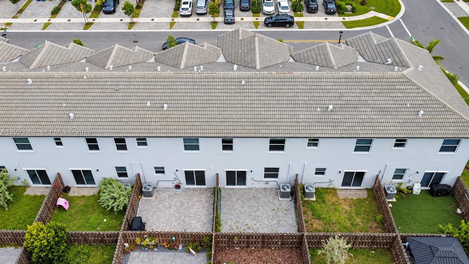 Multi-unit residential structure featuring a tiled roof, light-colored stucco exterior, sliding glass door access, paved patio areas, and private fenced backyards