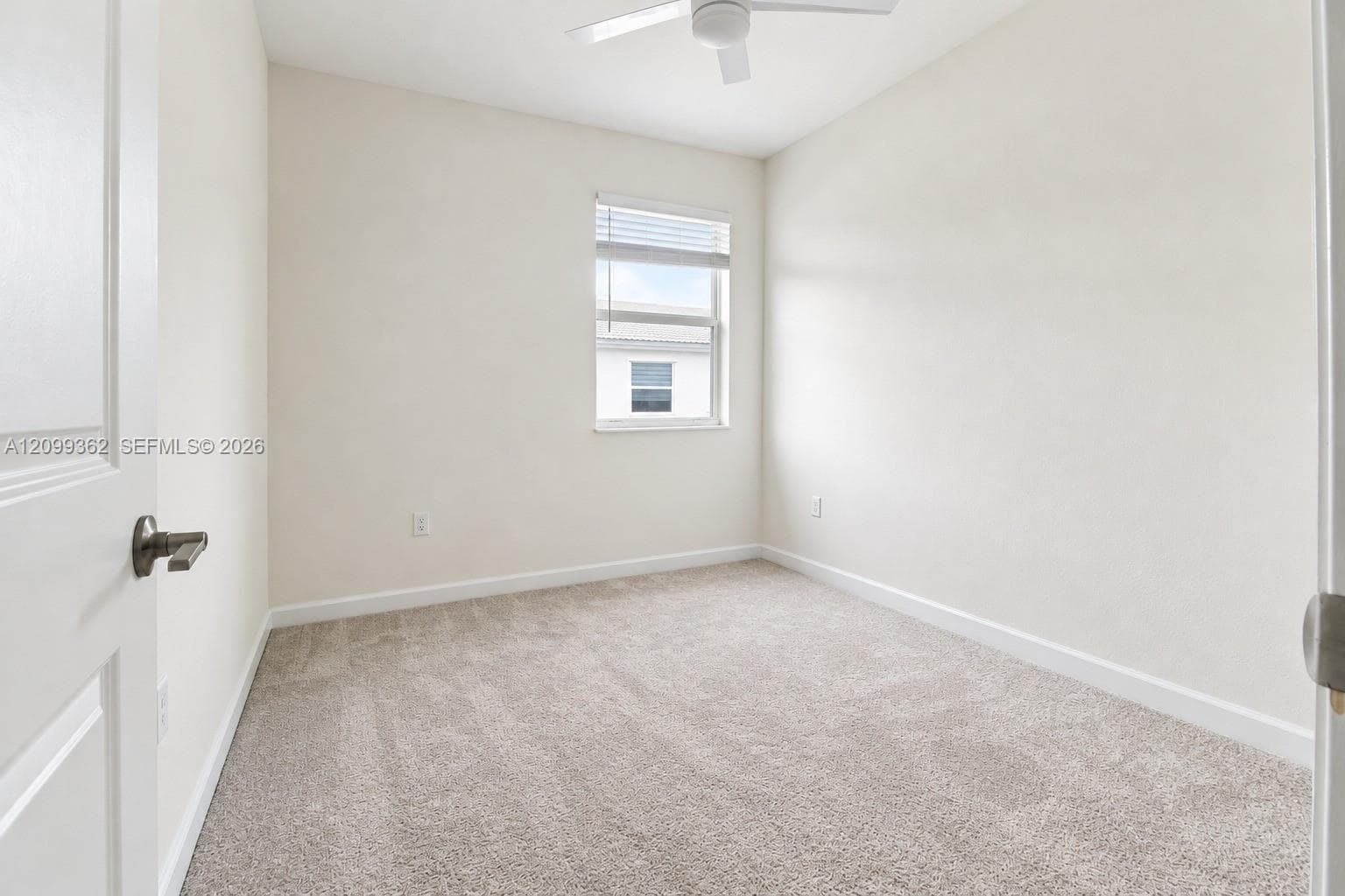 Neutral-toned room featuring neutral carpeting, a window with horizontal blinds, and a white ceiling fan